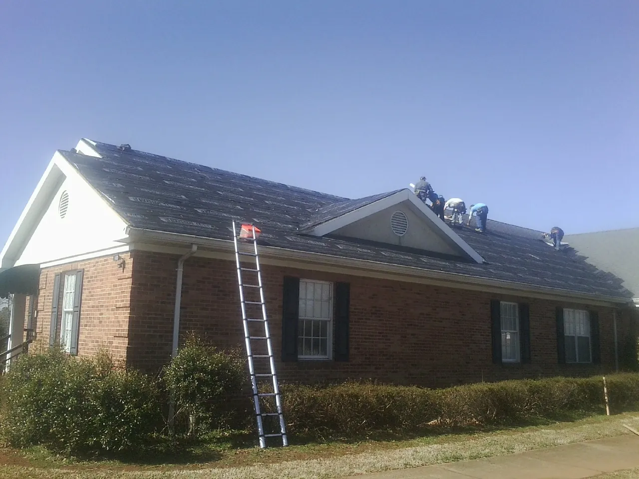 Crew tearing shingles off a brick ranch roof with a ladder set — Metal Roof Repair work by our crew in Marion